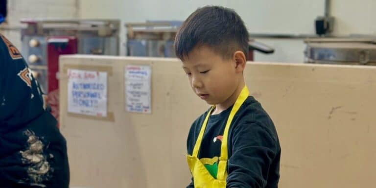 Young boy with a yellow apron engaged in a classroom activity.