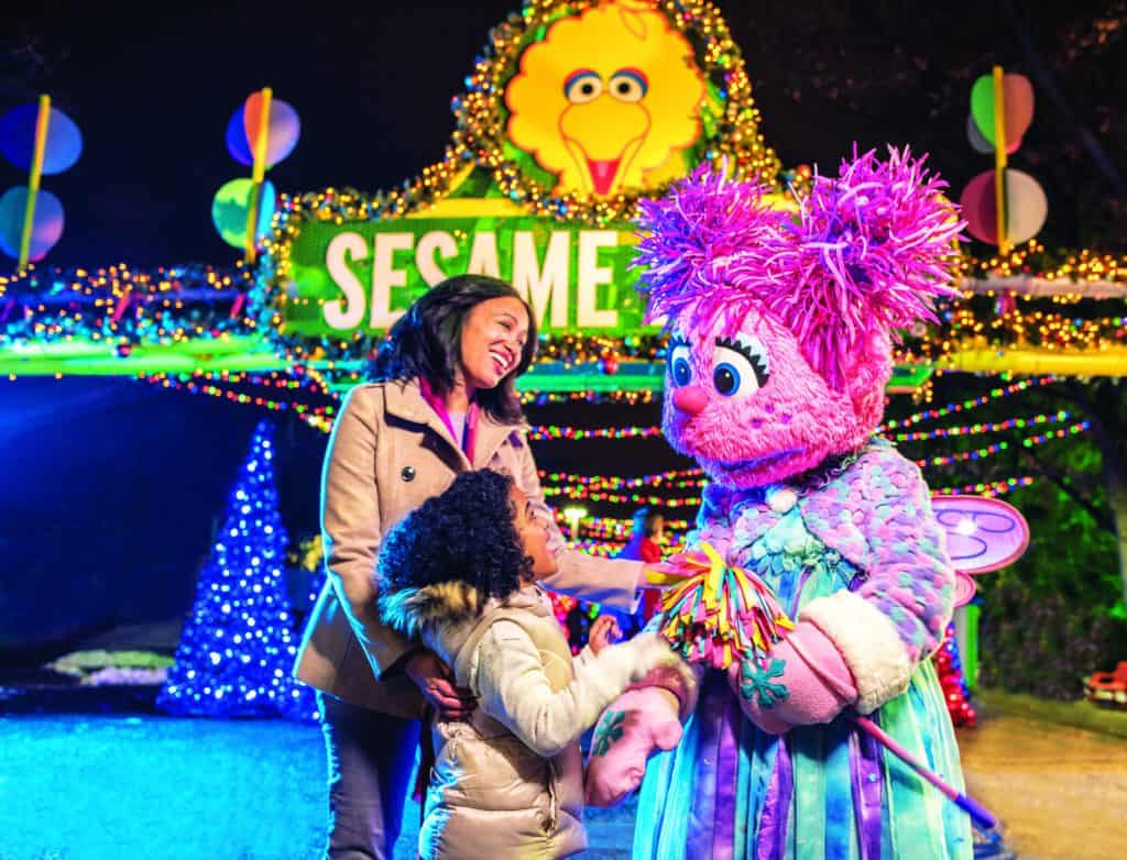 Children with Sesame Street characters at festive holiday event.
